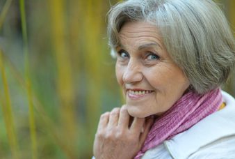 A woman with grey hair wearing a pink scarf.