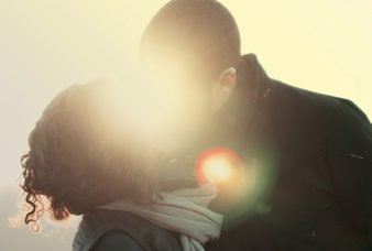 A man and woman kissing in the sunlight.