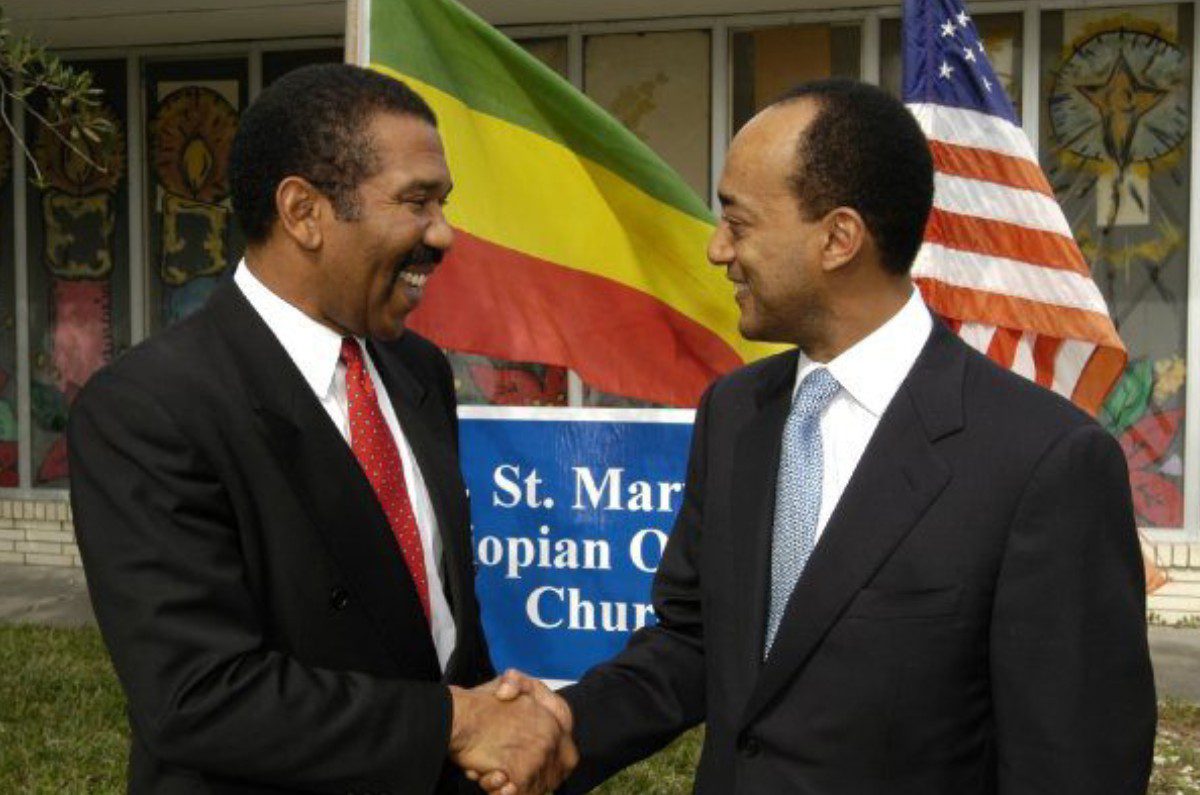Two men shaking hands in front of a church.